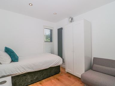 A bedroom with a single bed a wardrobe a gray chair and a window with shutters at Orchard Leigh in North Petherton
