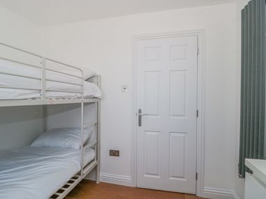 A small room with a metal bunk bed to the left a closed white door in the center and a gray vertical radiator on the right at Orchard Leigh in North Petherton