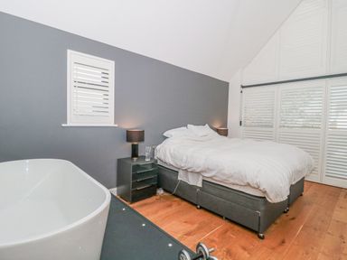 A bedroom with a bed bedside tables lamps a bathtub and dumbbells at Orchard Leigh in North Petherton