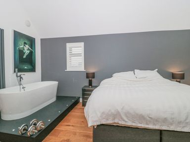 A bedroom with a bed and a bathtub on a raised platform with dumbbells at Orchard Leigh in North Petherton