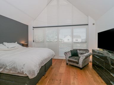 A bedroom with a bed a chair a dresser a television and large white shutters covering the window at Orchard Leigh in North Petherton