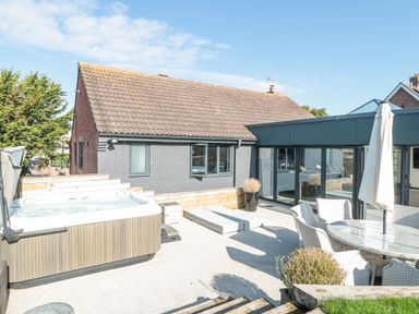 An outdoor patio with a hot tub dining table with chairs an umbrella and a sun lounger at Orchard Leigh in North Petherton