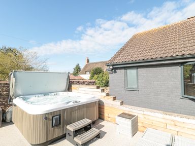 An outdoor hot tub with steps near a gray brick building and wooden fence at Orchard Leigh in North Petherton
