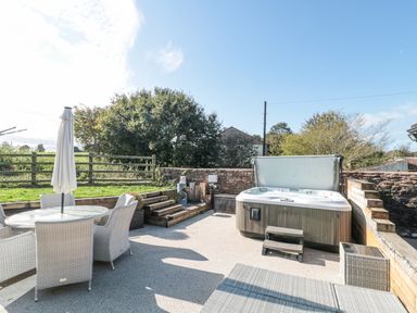 An outdoor patio with a hot tub wooden steps and a glass table with chairs at Orchard Leigh in North Petherton