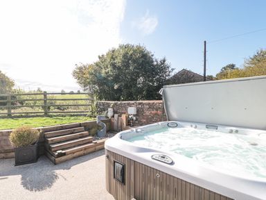 An outdoor hot tub on a patio with wooden steps leading to a grassy area and a wooden fence at Orchard Leigh in North Petherton