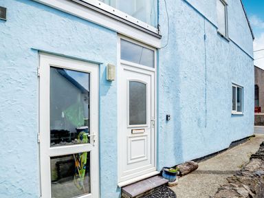 A light blue textured exterior wall with two white doors and a window at Victoria House in Rhosneigr