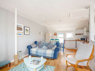 An open plan living room and kitchen with a blue sofa dining table and wooden armchair at Victoria House in Rhosneigr