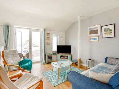 A living room with a blue sofa two wooden armchairs a TV on a stand a coffee table and framed pictures on the wall at Victoria House in Rhosneigr