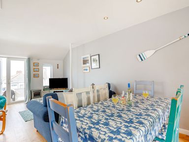 A dining area with a blue patterned tablecloth on a table with chairs and a living room with sofas and a television at Victoria House in Rhosneigr