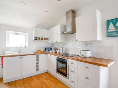 A kitchen with white cabinets wooden countertops a sink oven toaster microwave and a wall sign at Victoria House in Rhosneigr