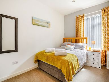 A bedroom with a bed a yellow blanket a bedside table with a lamp and window with orange curtains at Victoria House in Rhosneigr