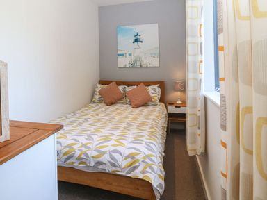 A bedroom with a bed a bedside table with a lamp a window and curtains at Victoria House in Rhosneigr