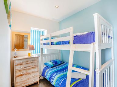 A bedroom with a white bunk bed with blue striped bedding and a wooden dresser with a lamp and glass of orange juice at Victoria House in Rhosneigr