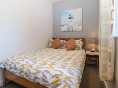 A bedroom with a bed table lamp and a window with curtains at Victoria House in Rhosneigr