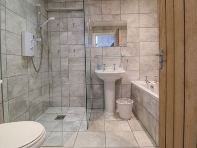 A bathroom with a shower, basin, bathtub, toilet, and a wicker basket at Victoria House in Rhosneigr