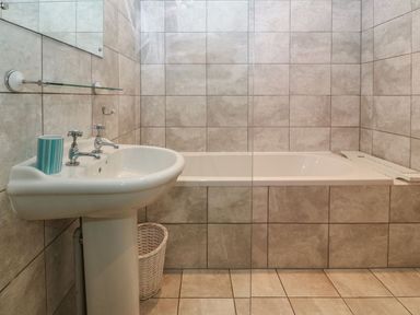 A bathroom with a pedestal sink and a bathtub surrounded by tiled walls Victoria House Rhosneigr