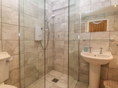 A bathroom with a tiled walk-in shower glass panels a sink with taps a mirror a toilet and a basket at Victoria House in Rhosneigr