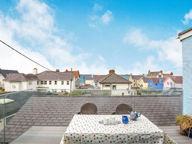 A rooftop terrace with a table covered by a polka dot tablecloth and two chairs overlooking houses and the sea at Victoria House in Rhosneigr