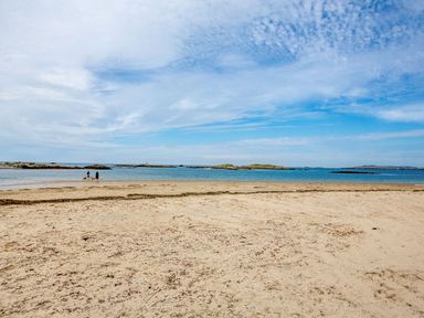A sandy beach with a few people near the water and small islands in the distance at Victoria House in Rhosneigr