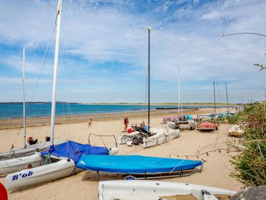 A sandy beach with multiple small sailboats and people near the shoreline at Victoria House in Rhosneigr
