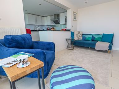A living room with blue armchair striped pouf and sofa and an open kitchen at Manhattan Beach in Castletown Portland
