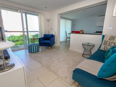 A living room with a blue armchair a blue sofa and a small round table near sliding glass doors at Manhattan Beach in Castletown Portland