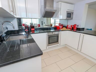 A kitchen with white cabinets black countertops and red appliances at Manhattan Beach in Castletown Portland