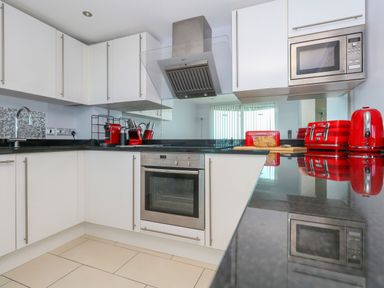 A kitchen with white cabinets black countertops and red appliances at Manhattan Beach in Castletown Portland