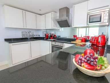 A modern kitchen with white cabinets black countertops red appliances and a bowl of fruit on the counter at Manhattan Beach in Castletown Portland