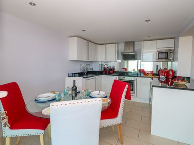 A kitchen with white cabinets red appliances and a glass dining table with red and white chairs at Manhattan Beach in Castletown Portland