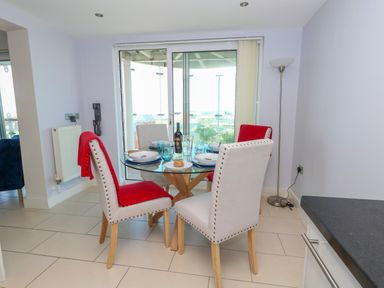 A dining area with a glass table set for four with plates and glasses and four padded chairs near glass sliding doors at Manhattan Beach in Castletown Portland