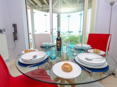 A dining area with a glass table and chairs set with plates and bread at Manhattan Beach in Castletown Portland