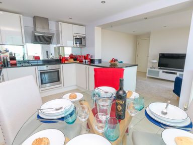 A dining table set with plates glasses and bread in a kitchen with white cabinets and red appliances at Manhattan Beach in Castletown Portland