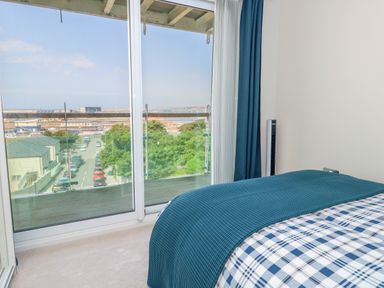 A bedroom with a bed facing a glass sliding door overlooking a street and distant buildings at Manhattan Beach in Castletown Portland