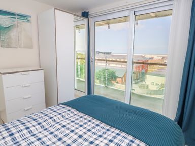A bedroom with a bed plaid bedding chest of drawers and wardrobe next to sliding glass door with balcony and a view at Manhattan Beach in Castletown Portland