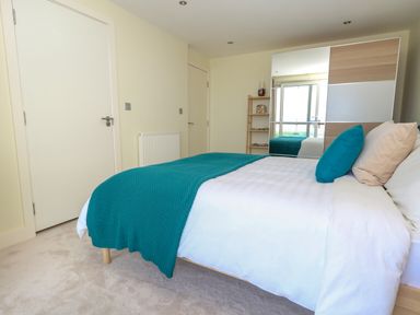 A bedroom with a bed with turquoise bedding and pillows a mirrored wardrobe a wooden shelf and two closed doors at Manhattan Beach in Castletown Portland