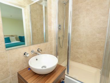 A bathroom with a round sink on a wooden cabinet and a glass shower enclosure at Manhattan Beach in Castletown Portland