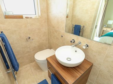 A bathroom with a white toilet a round sink on a wooden cabinet blue towels on a towel rack and beige tiled walls at Manhattan Beach Castletown Portland