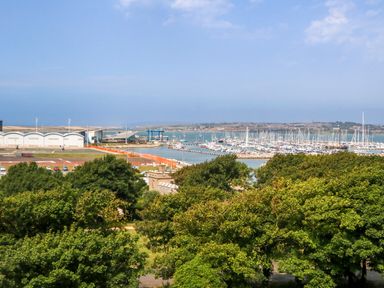 A marina with boats docked near a building and trees in the foreground at Manhattan Beach Castletown Portland
