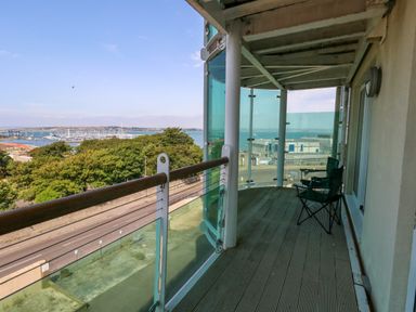 A balcony with two folding chairs and a glass railing overlooking trees road and a marina at Manhattan Beach in Castletown Portland