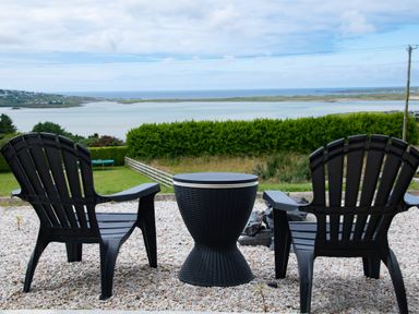 Two black chairs with a round black table on a gravel patio overlooking a bay with green grass and hedges at Ballyness Bay in Killult Upper near Gortahork County Donegal