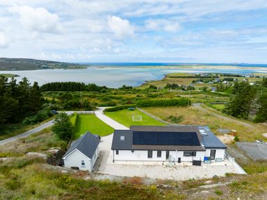 A white house with solar panels on the roof near a body of water with hills in the background at Ballyness Bay in Killult Upper near Gortahork County Donegal
