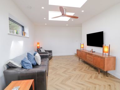 A living room with two dark leather sofas a wooden media cabinet with lamps and a wall mounted TV at Ballyness Bay in Killult Upper near Gortahork County Donegal