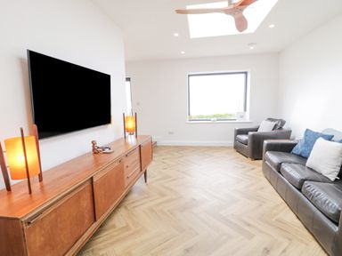A living room with a wall-mounted TV wooden sideboard two table lamps a leather sofa and armchair at Ballyness Bay in Killult Upper near Gortahork County Donegal