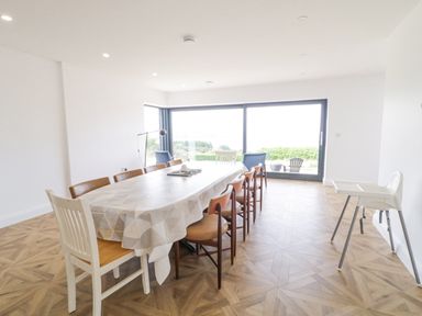 A dining room with a long table covered by a tablecloth surrounded by chairs and a high chair near a large window at Ballyness Bay in Killult Upper near Gortahork County Donegal
