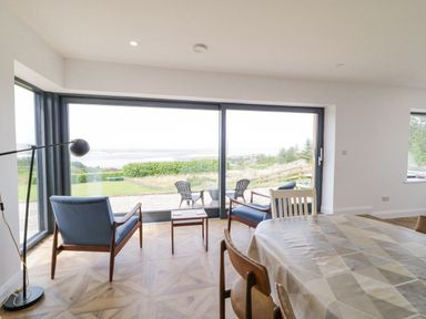 A dining room with a table and chairs next to large glass windows showing chairs outside at Ballyness Bay in Killult Upper near Gortahork County Donegal