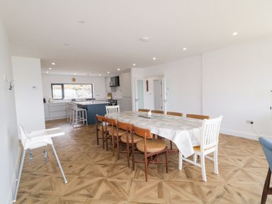A dining room with a long table covered with a tablecloth surrounded by chairs next to a kitchen with stools at Ballyness Bay in Killult Upper near Gortahork County Donegal