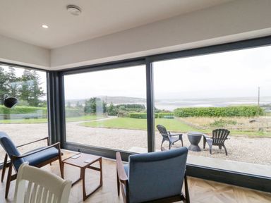 A seating area with two blue chairs a wooden table and large windows overlooking a garden and distant hills at Ballyness Bay in Killult Upper near Gortahork County Donegal