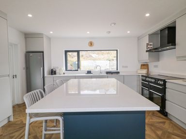 A kitchen with a large island and gray chairs a stainless steel fridge and oven with cabinets at Ballyness Bay in Killult Upper near Gortahork County Donegal