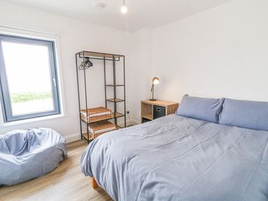 A bedroom with a double bed covered with gray bedding a bean bag a metal and wood shelving unit with wicker baskets a wooden side table with a lamp and a window at Ballyness Bay in Killult Upper near Gortahork County Donegal